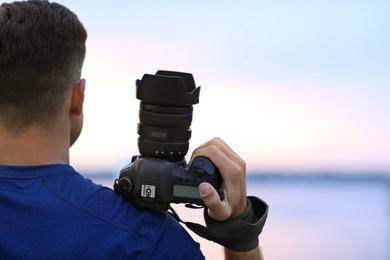 Photographer with professional camera near river at sunset, closeup