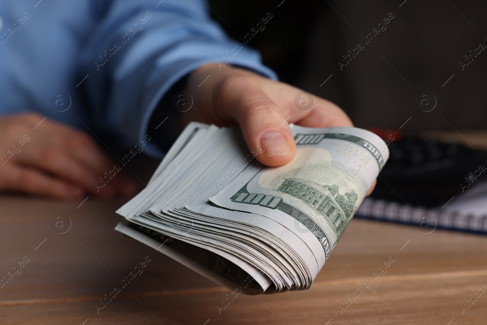 Photo of Money exchange. Woman holding dollar banknotes at wooden table, closeup