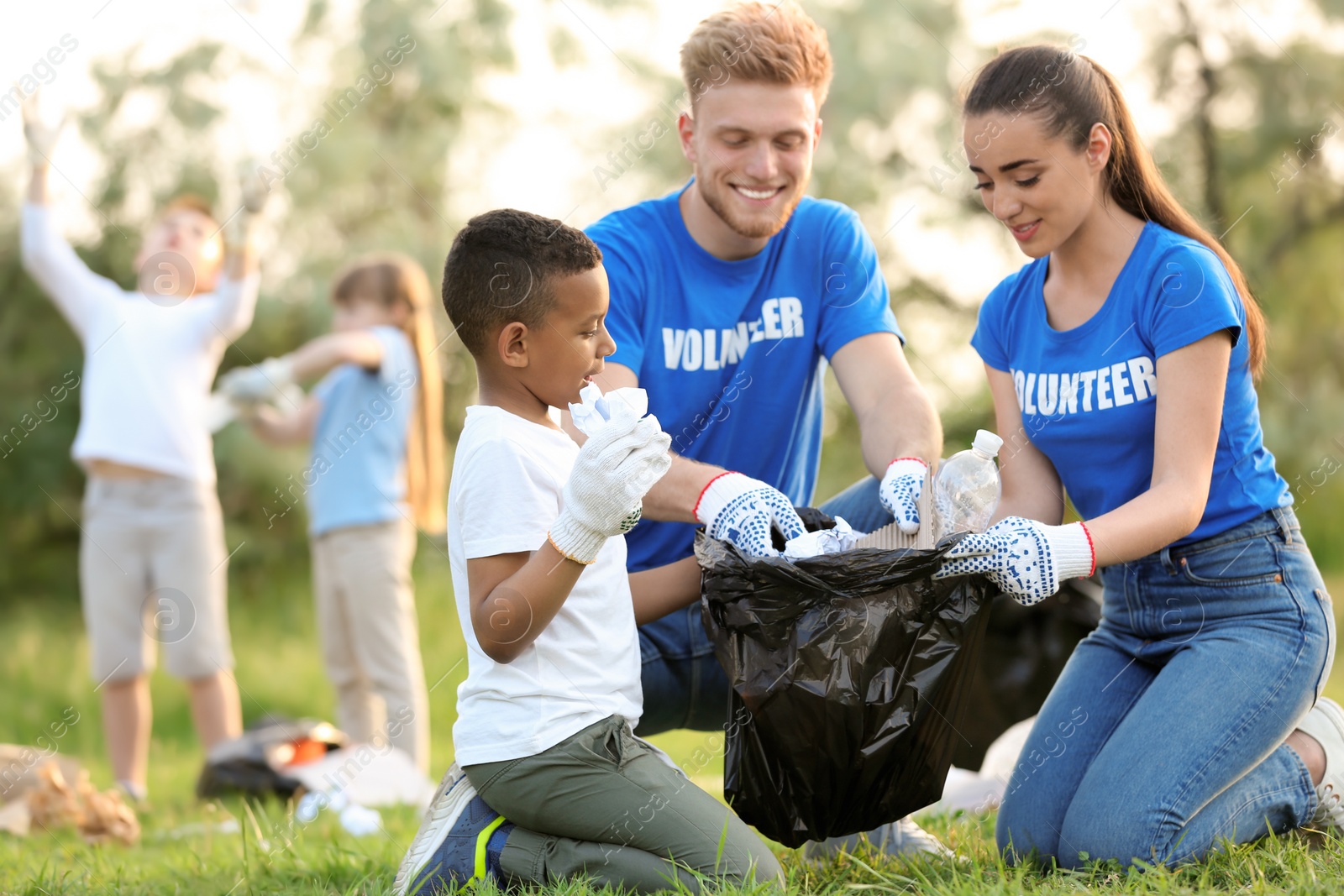 Photo of Little African-American boy collecting trash with volunteers in park