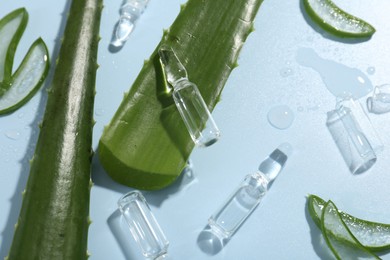 Skincare ampoules with extract of aloe vera and green leaves on light blue background, closeup