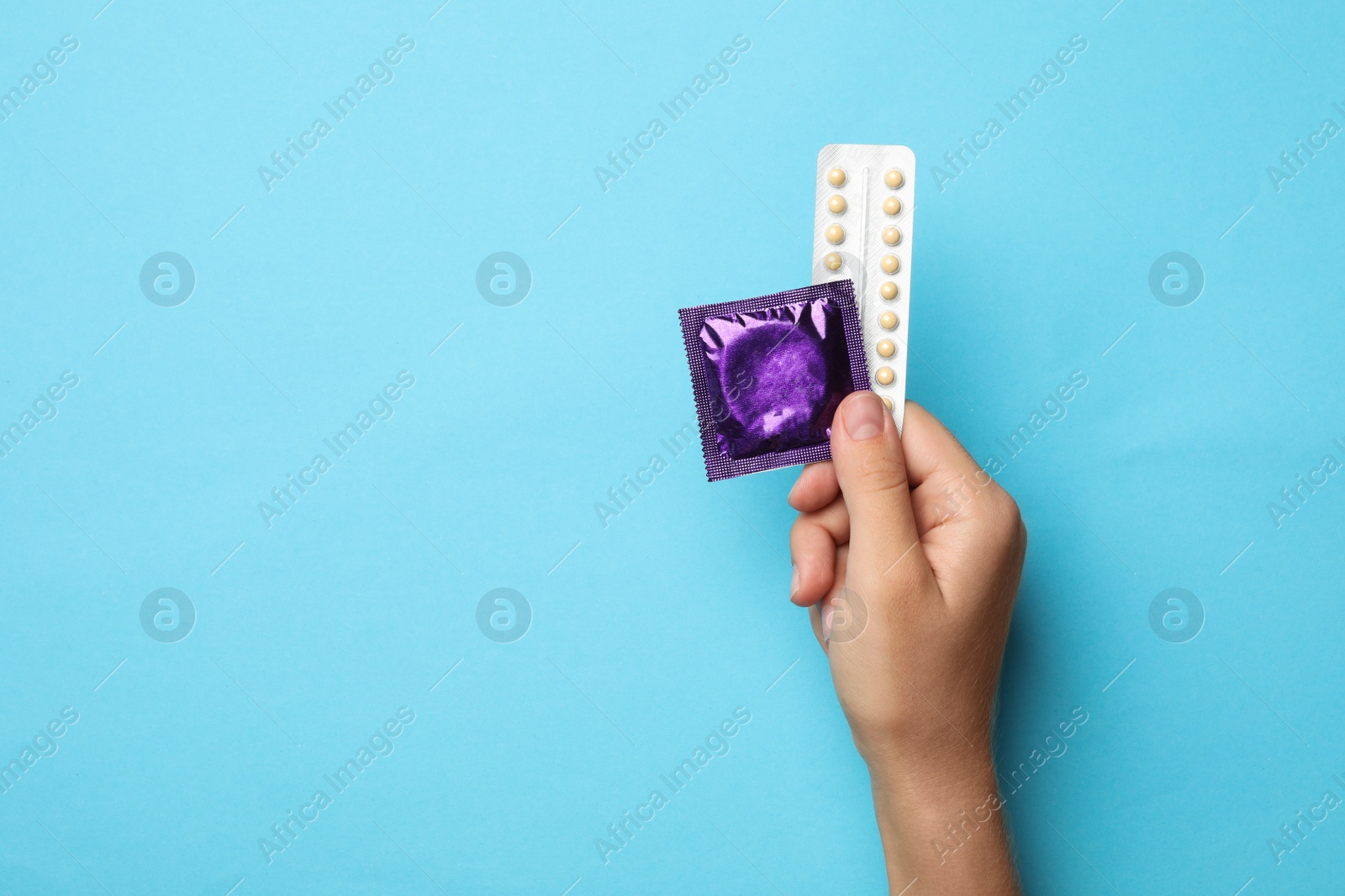 Photo of Woman holding condom and birth control pills on blue background, top view with space for text. Safe sex