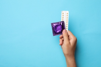 Photo of Woman holding condom and birth control pills on blue background, top view with space for text. Safe sex