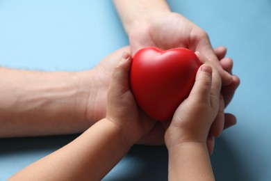 Photo of Father and his child holding red decorative heart on light blue background, closeup