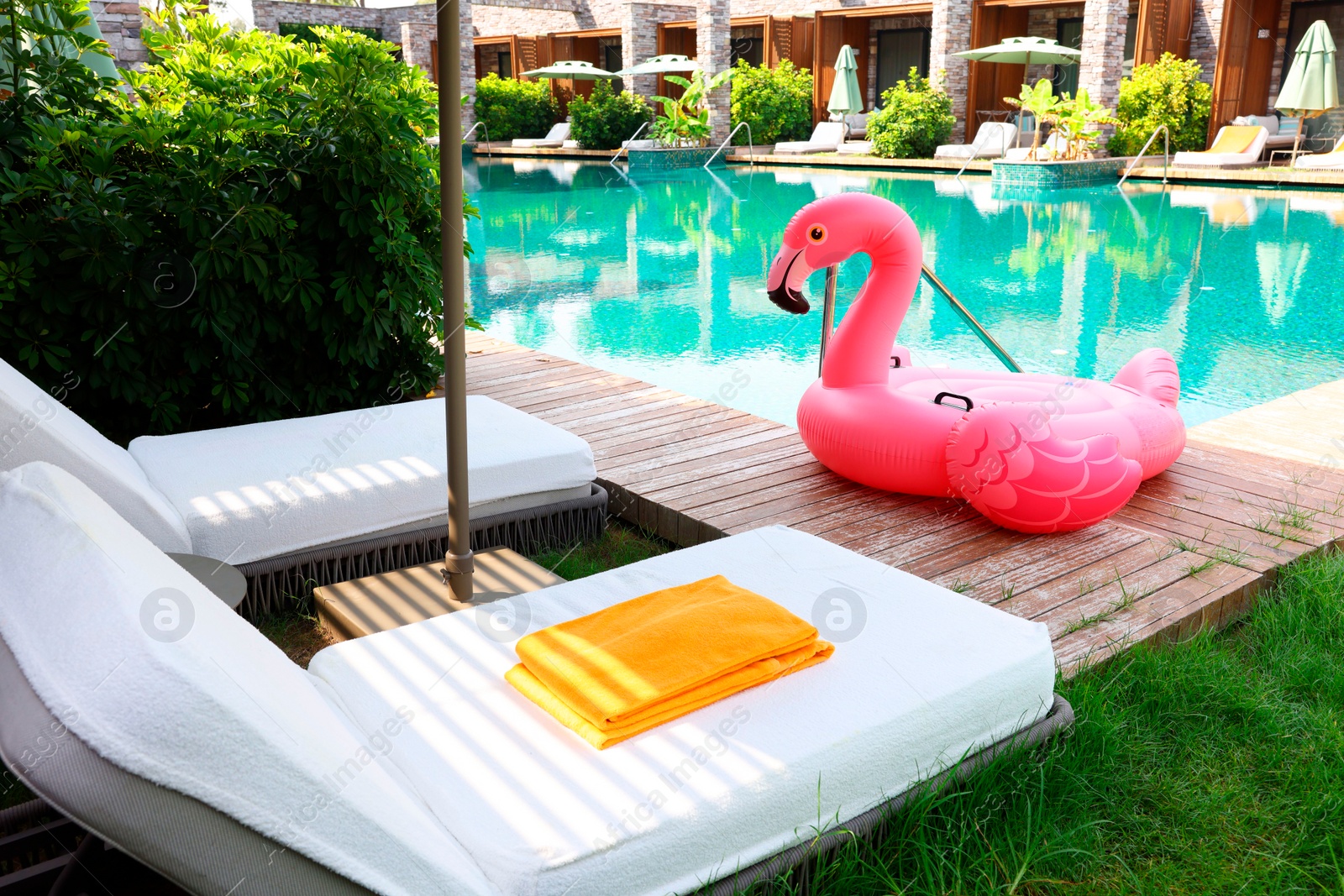 Photo of Float in shape of flamingo on wooden deck near swimming pool and sunbeds at luxury resort