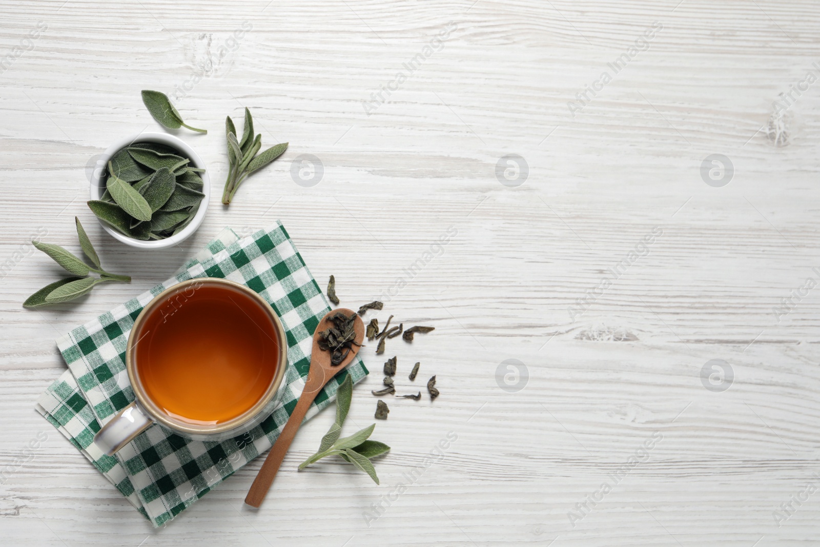 Photo of Cup of sage tea, green leaves and spoon on white wooden table, flat lay. Space for text