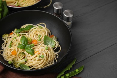 Photo of Delicious pasta primavera with basil, broccoli and peas served on grey wooden table, closeup. Space for text
