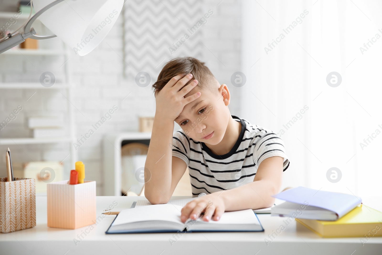 Photo of Little boy suffering from headache while doing homework at table indoors