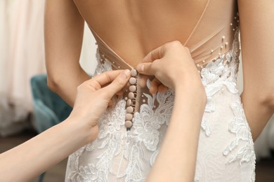 Woman helping bride wear wedding dress in boutique, closeup