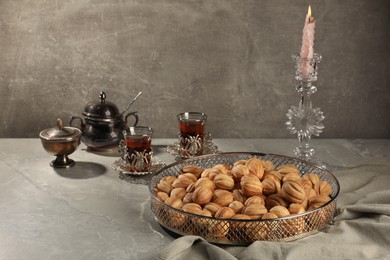 Photo of Delicious walnut shaped cookies, burning candle and glasses of tea on grey table, space for text. Tasty pastry with filling carrying nostalgic home atmosphere