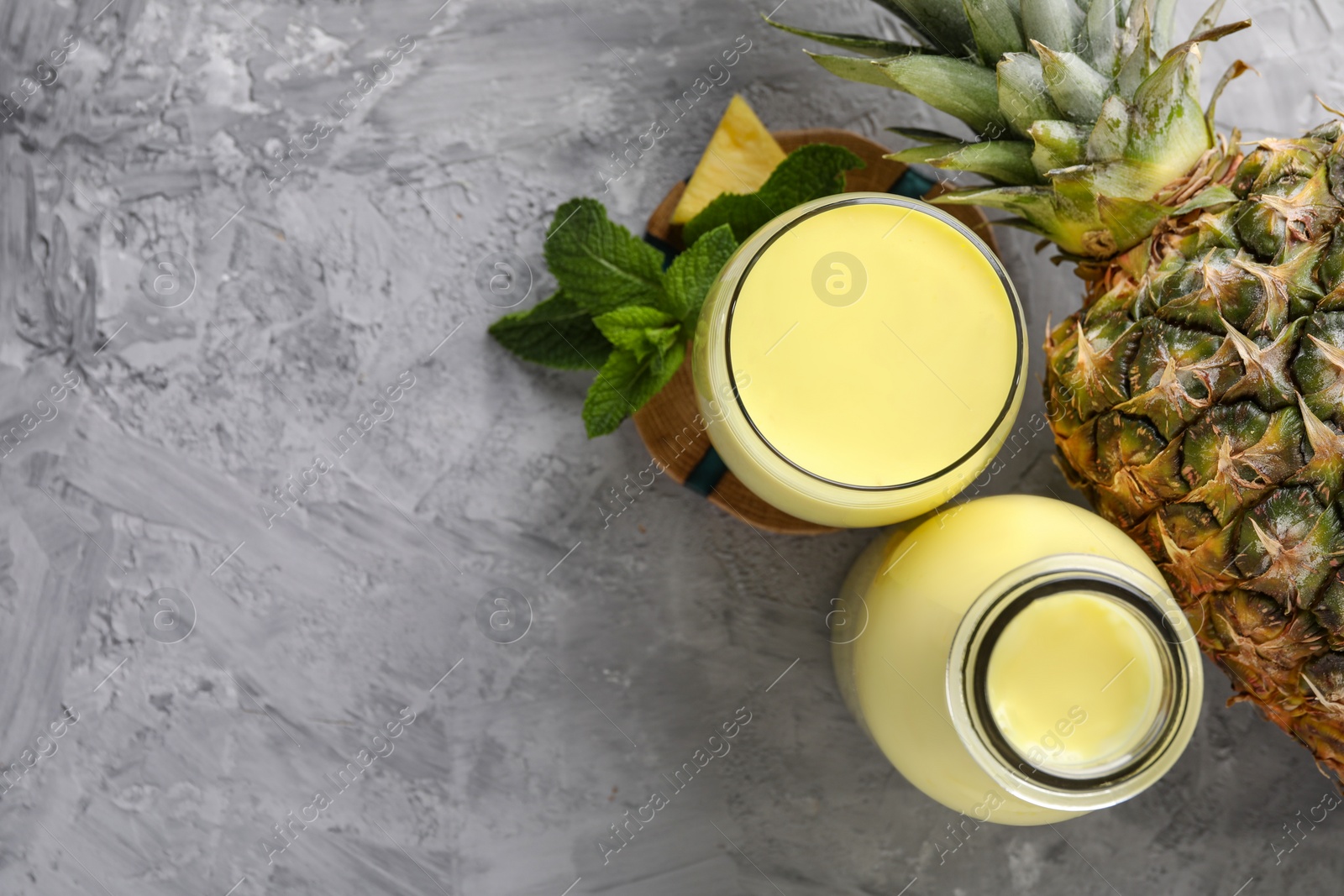 Photo of Tasty pineapple smoothie, mint and fruit on grey textured table, flat lay. Space for text