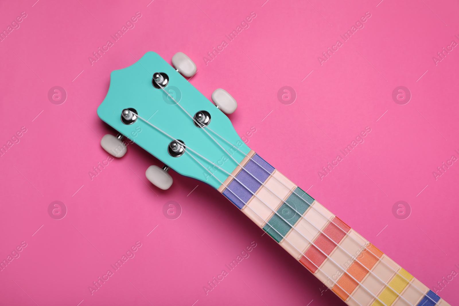 Photo of Colorful ukulele neck on pink background, top view. String musical instrument