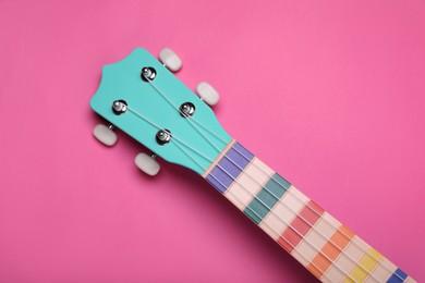 Colorful ukulele neck on pink background, top view. String musical instrument