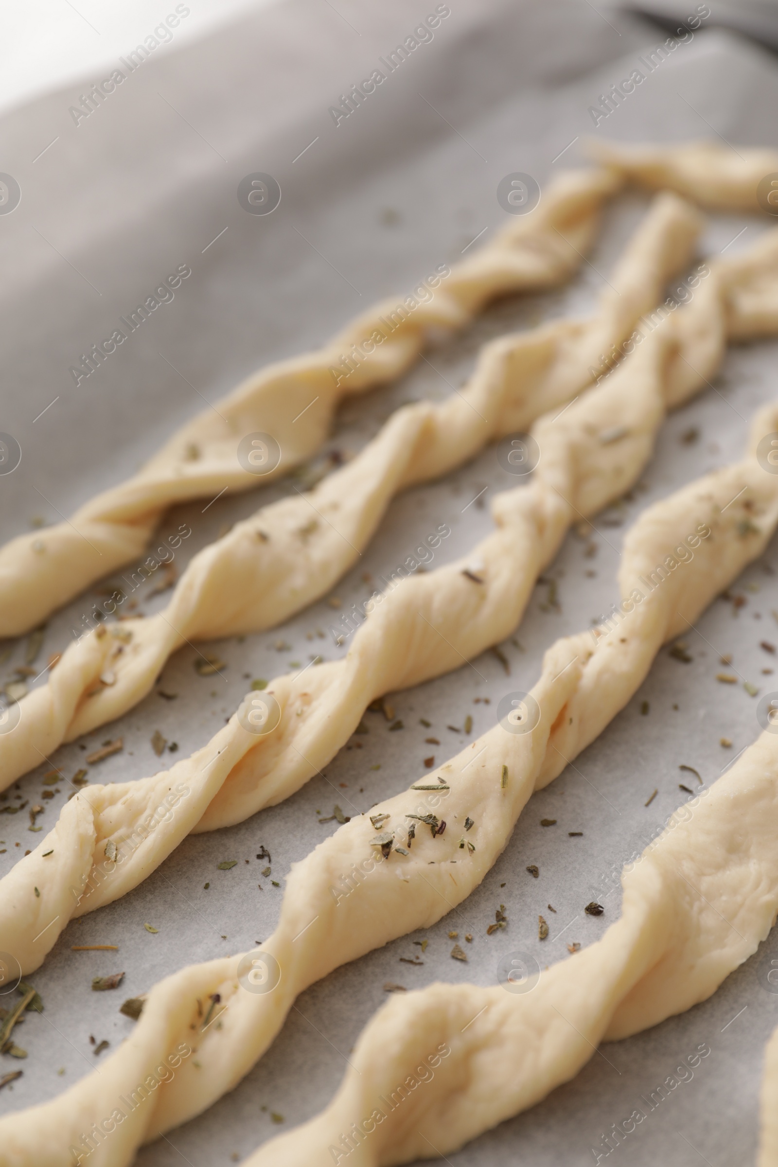 Photo of Homemade breadsticks with spices on baking sheet, closeup. Cooking traditional grissini