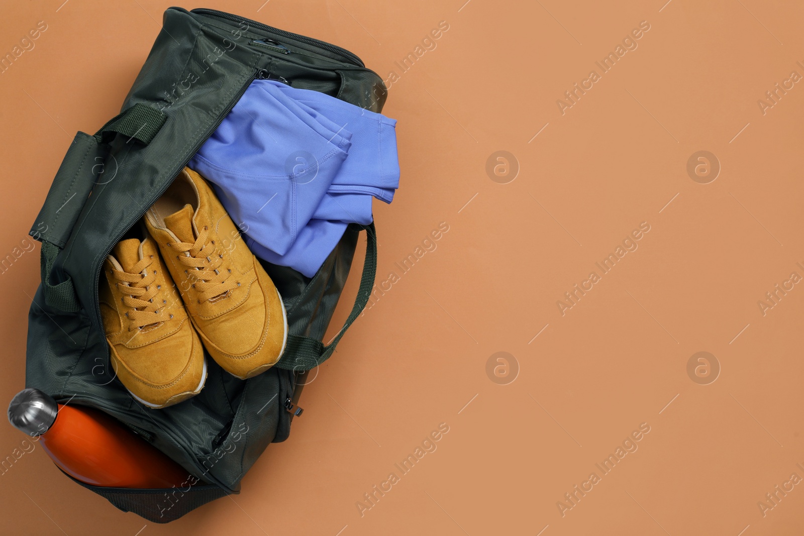 Photo of Sports bag with sneakers, clothes and bottle on pale brown background, top view. Space for text