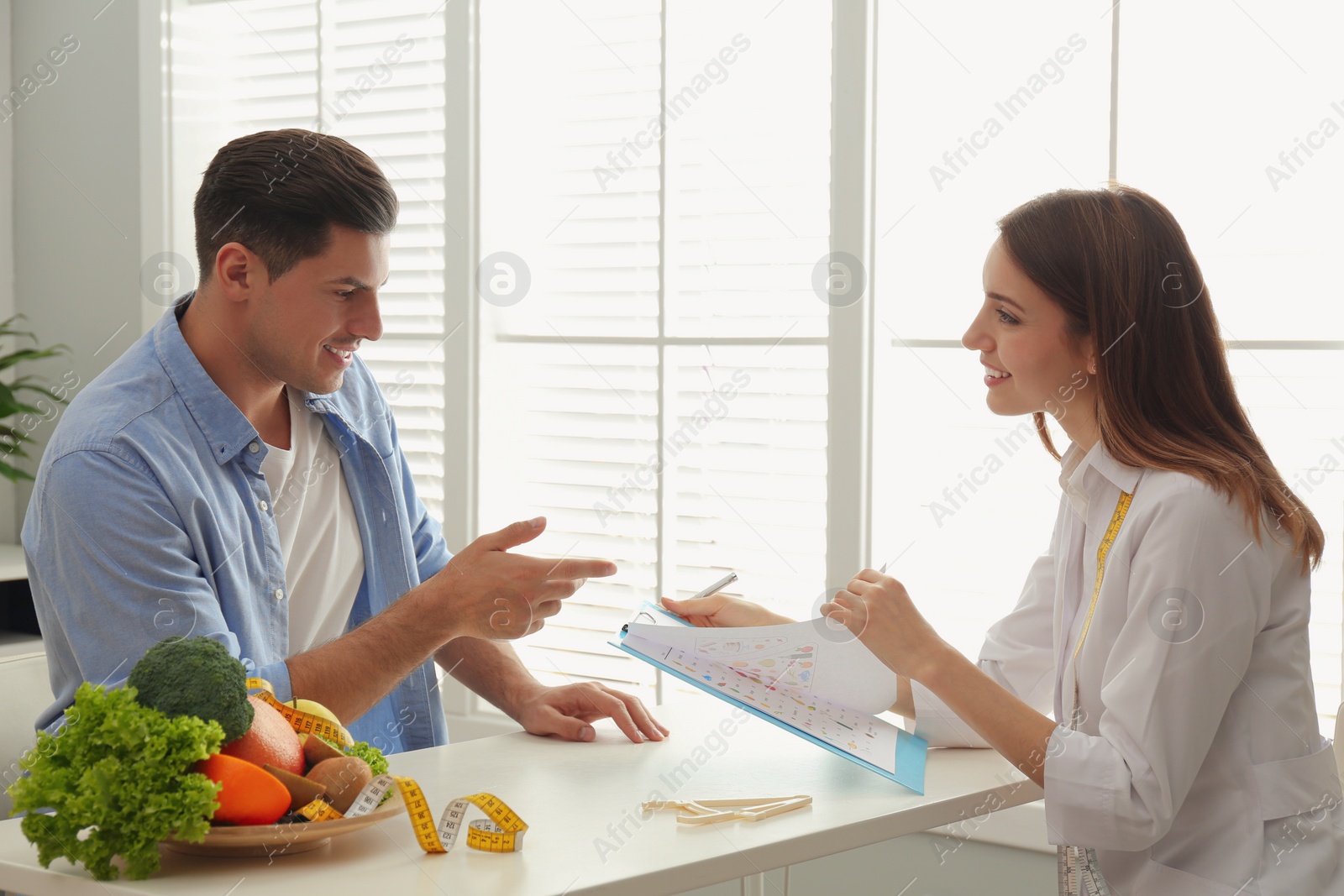 Photo of Young nutritionist consulting patient at table in clinic