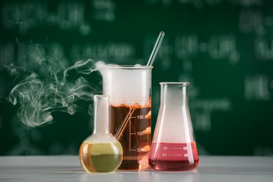 Photo of Laboratory glassware with colorful liquids on white table. Chemical reaction