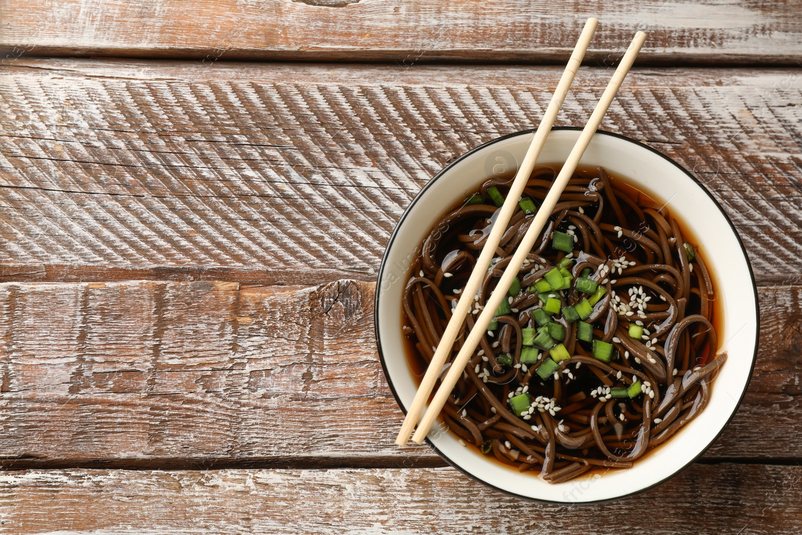 Photo of Tasty soup with buckwheat noodles (soba), onion in bowl and chopsticks on wooden table, top view. Space for text