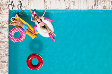Image of Happy couple with inflatable rings and mattress in swimming pool, top view. Summer vacation