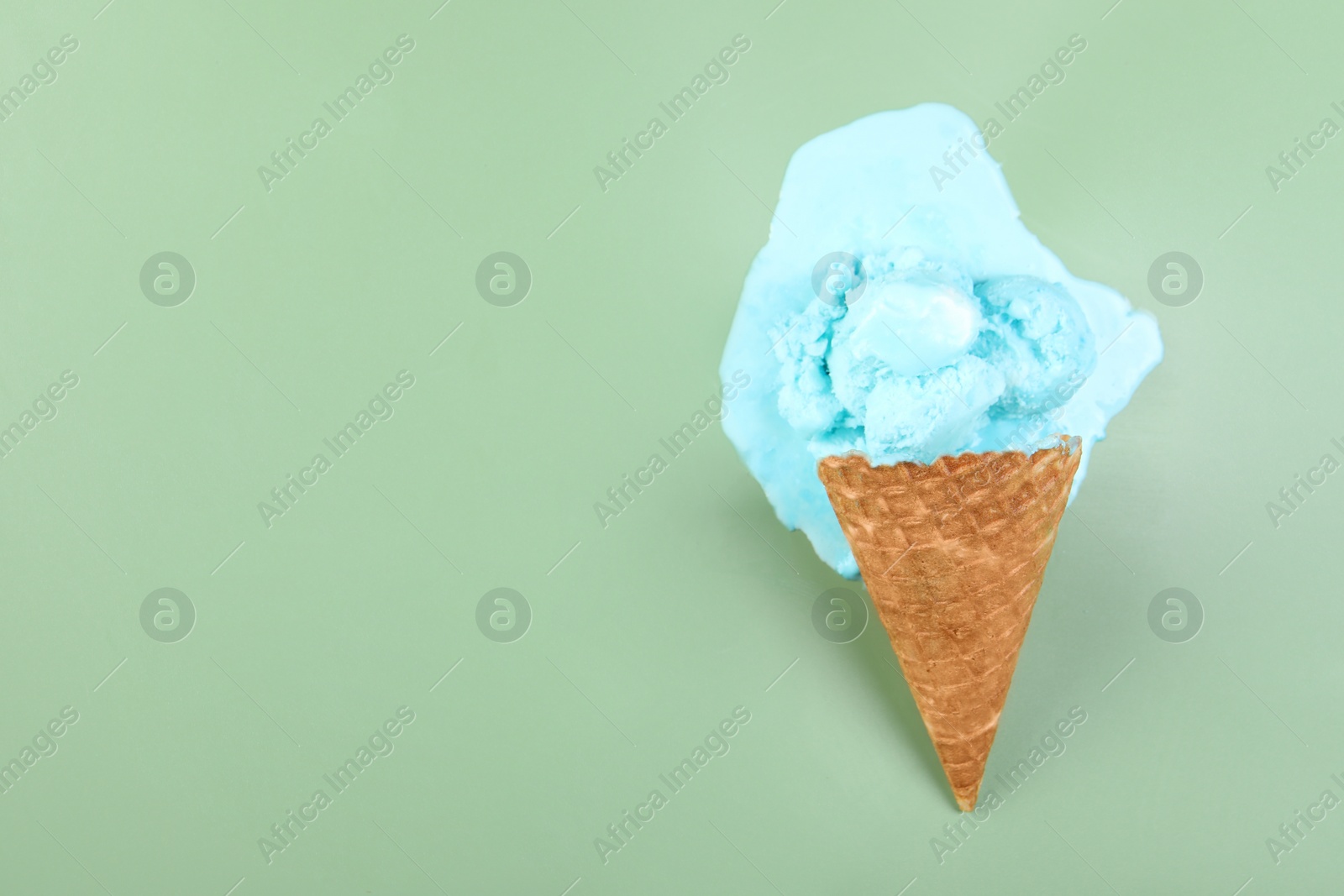 Photo of Melted ice cream and wafer cone on green background, top view. Space for text