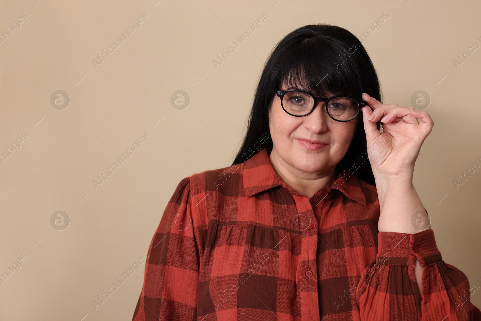 Photo of Beautiful overweight mature woman in eyeglasses on beige background. Space for text