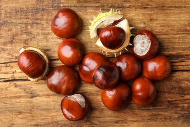 Photo of Many horse chestnuts on wooden table, flat lay