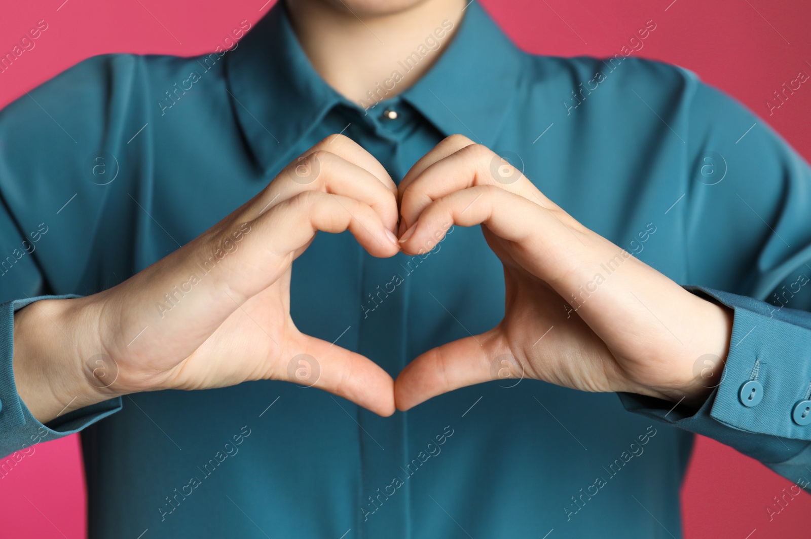 Photo of Woman making heart with her hands on pink background, closeup