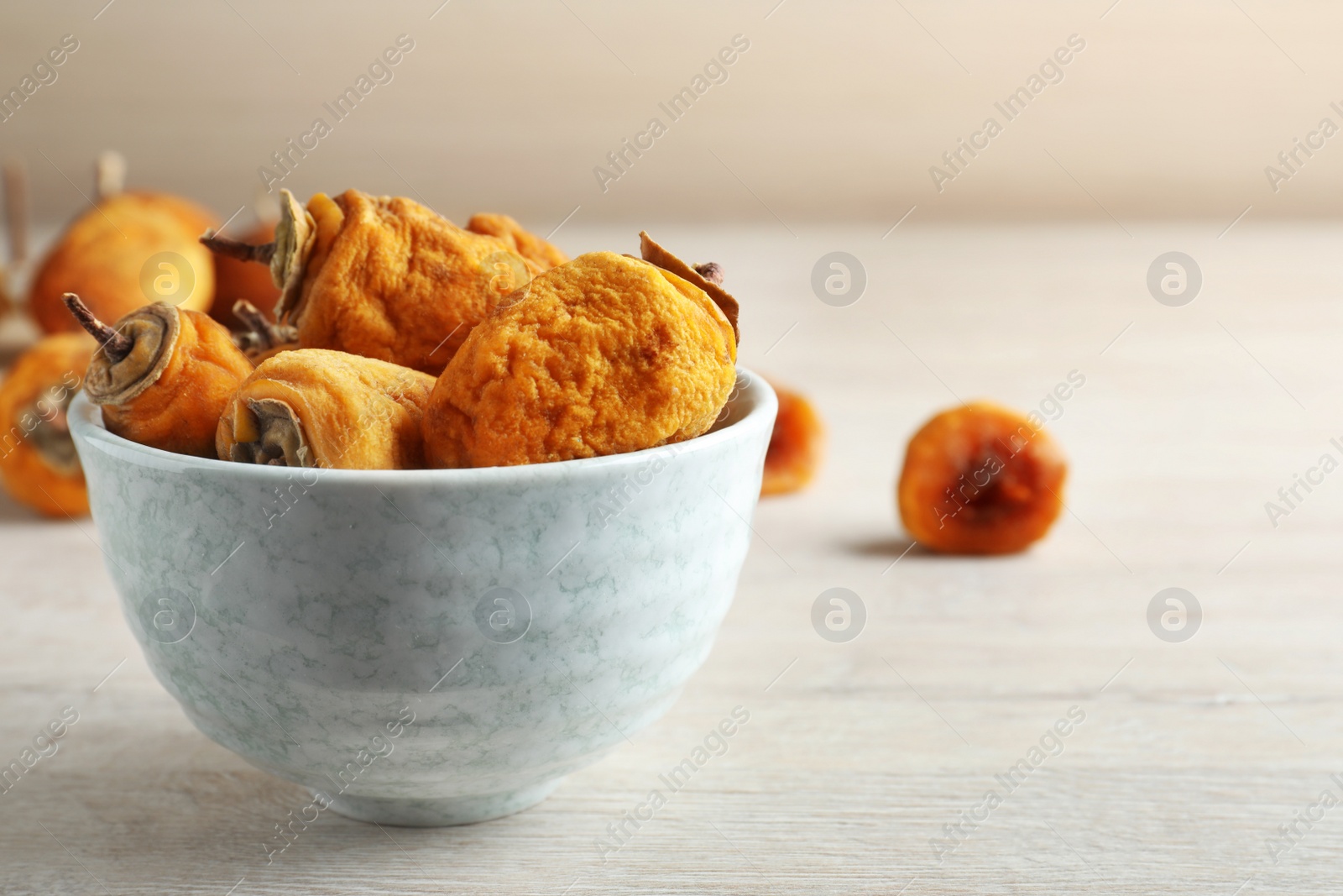 Photo of Bowl with tasty dried persimmon fruits on wooden table, space for text