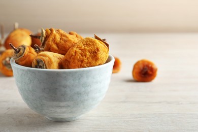 Bowl with tasty dried persimmon fruits on wooden table, space for text
