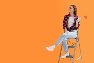 Photo of Designer with roller sitting on folding ladder near freshly painted orange wall, space for text