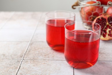 Photo of Tasty pomegranate juice in glasses on white tiled table. Space for text