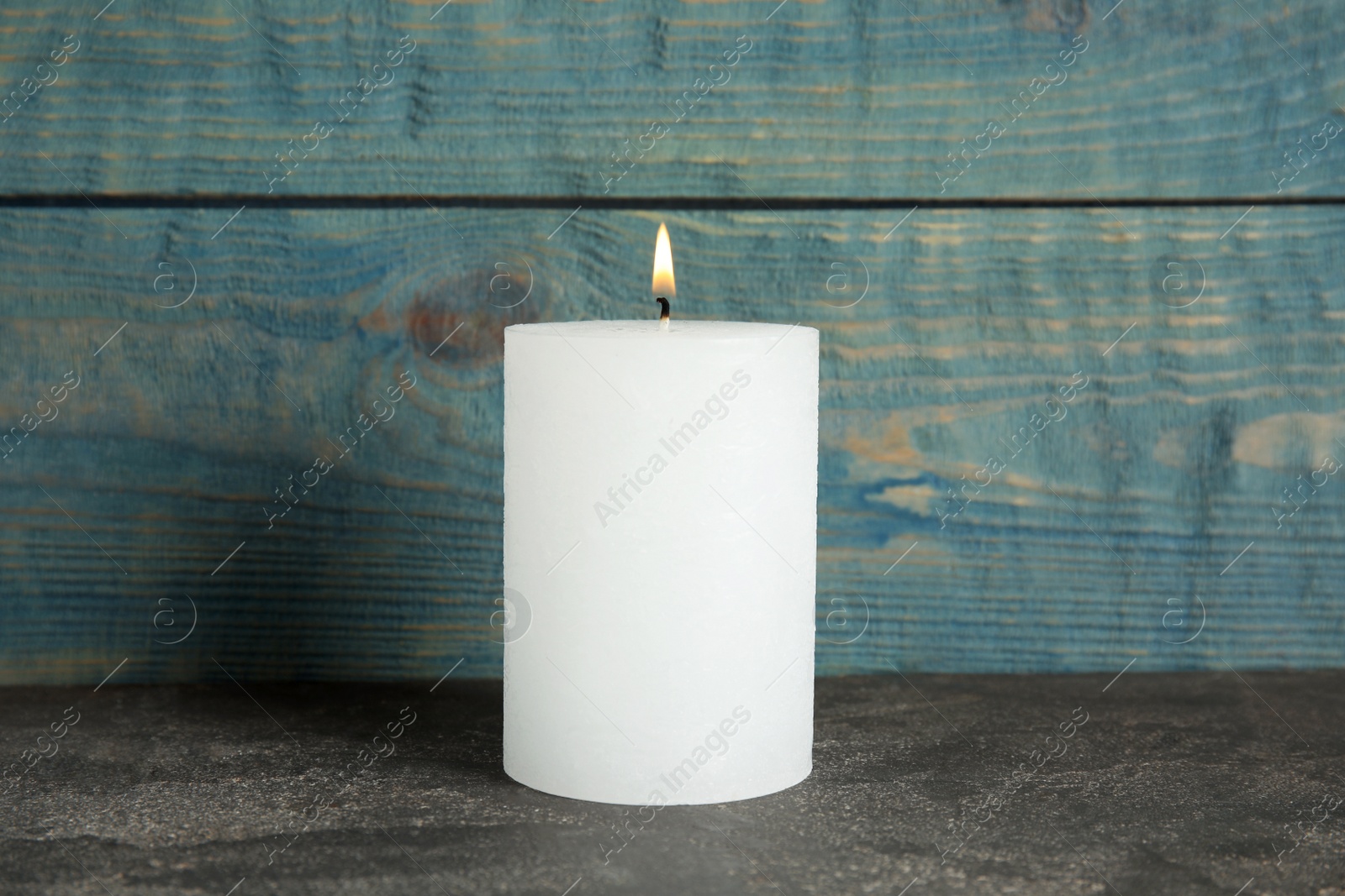 Photo of Alight wax candle on table against wooden background
