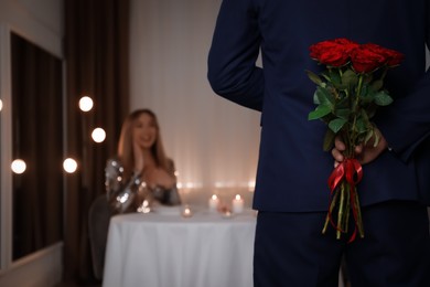 Photo of Man hiding roses for his beloved woman in restaurant at romantic dinner