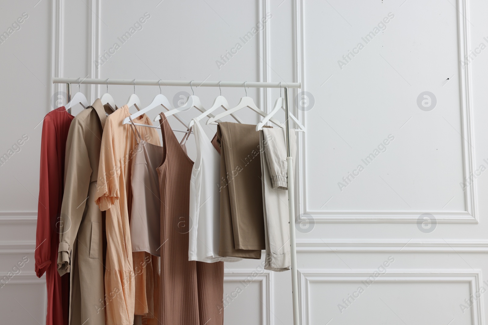 Photo of Rack with different stylish women`s clothes near white wall indoors, space for text