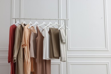 Rack with different stylish women`s clothes near white wall indoors, space for text