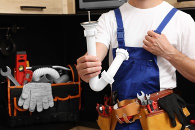 Photo of Professional plumber with corrugated pipe and tool belt indoors, closeup
