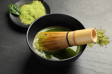Photo of Cup of fresh matcha tea with bamboo whisk on black table, closeup