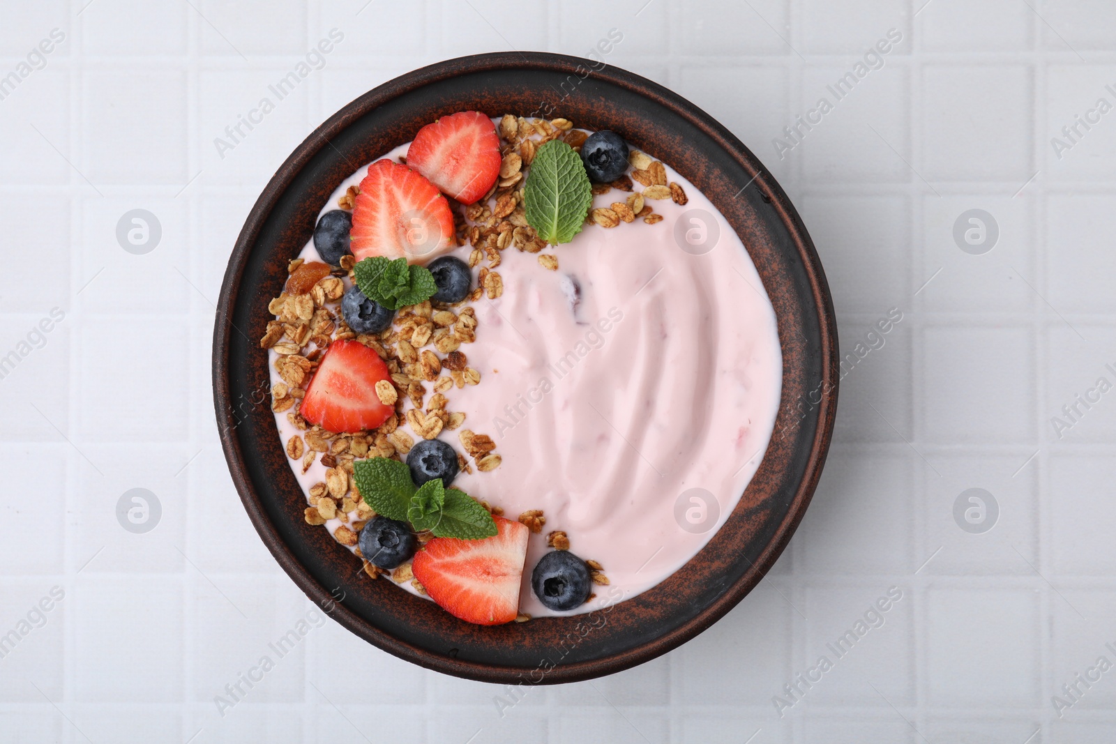 Photo of Bowl with yogurt, berries and granola on white tiled table, top view