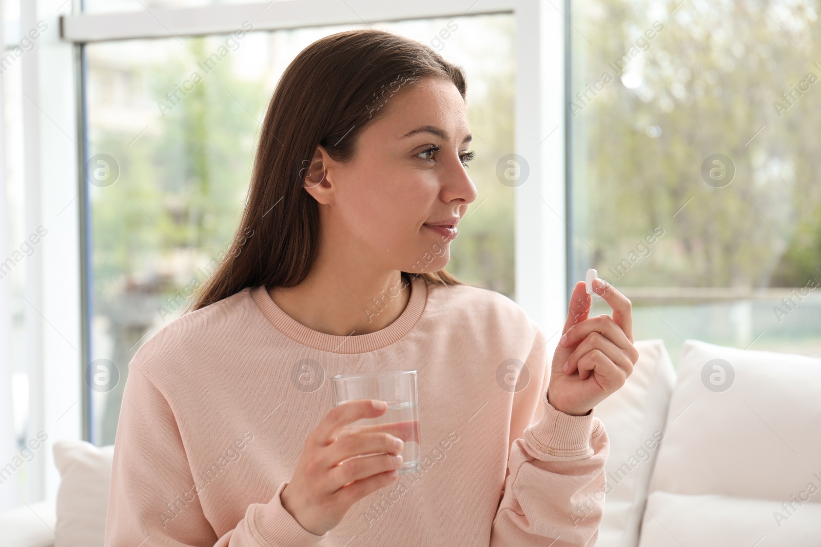 Photo of Young woman with glass of water taking pill at home