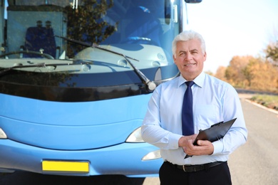 Photo of Professional driver with clipboard near bus. Passenger transportation