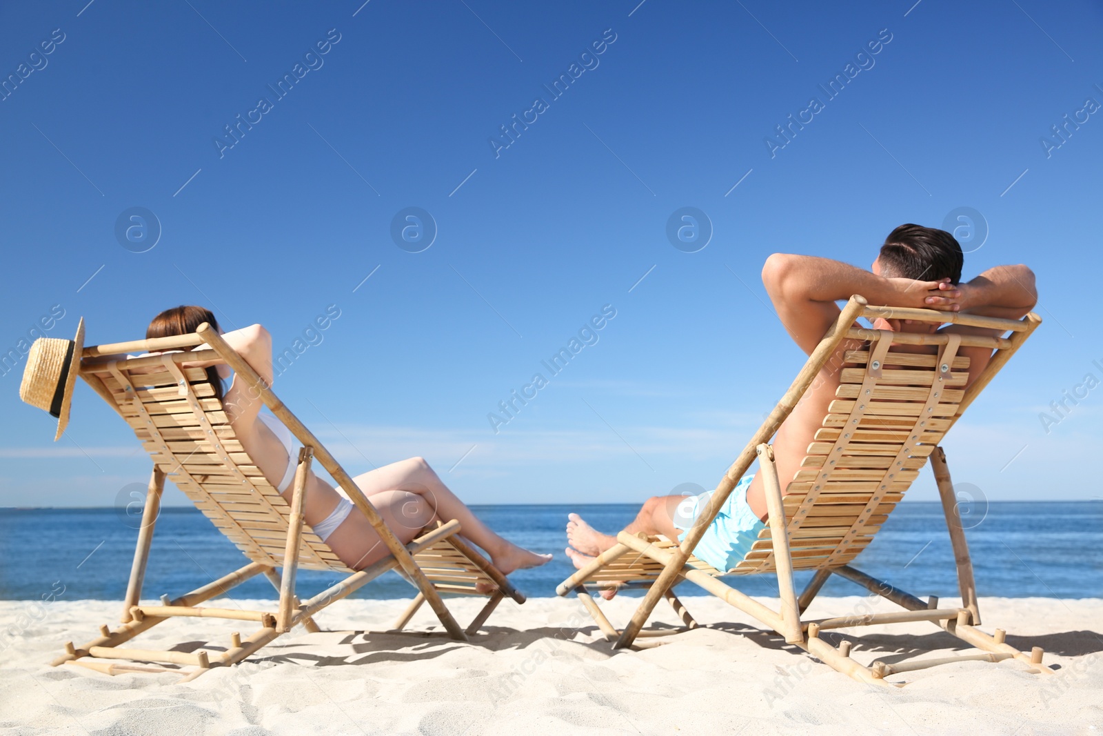 Photo of Woman in bikini and her boyfriend on deck chairs at beach. Lovely couple