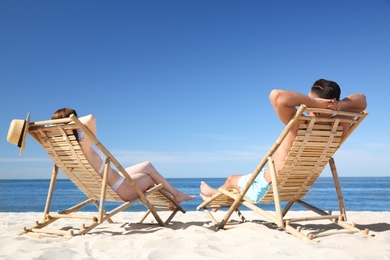 Woman in bikini and her boyfriend on deck chairs at beach. Lovely couple