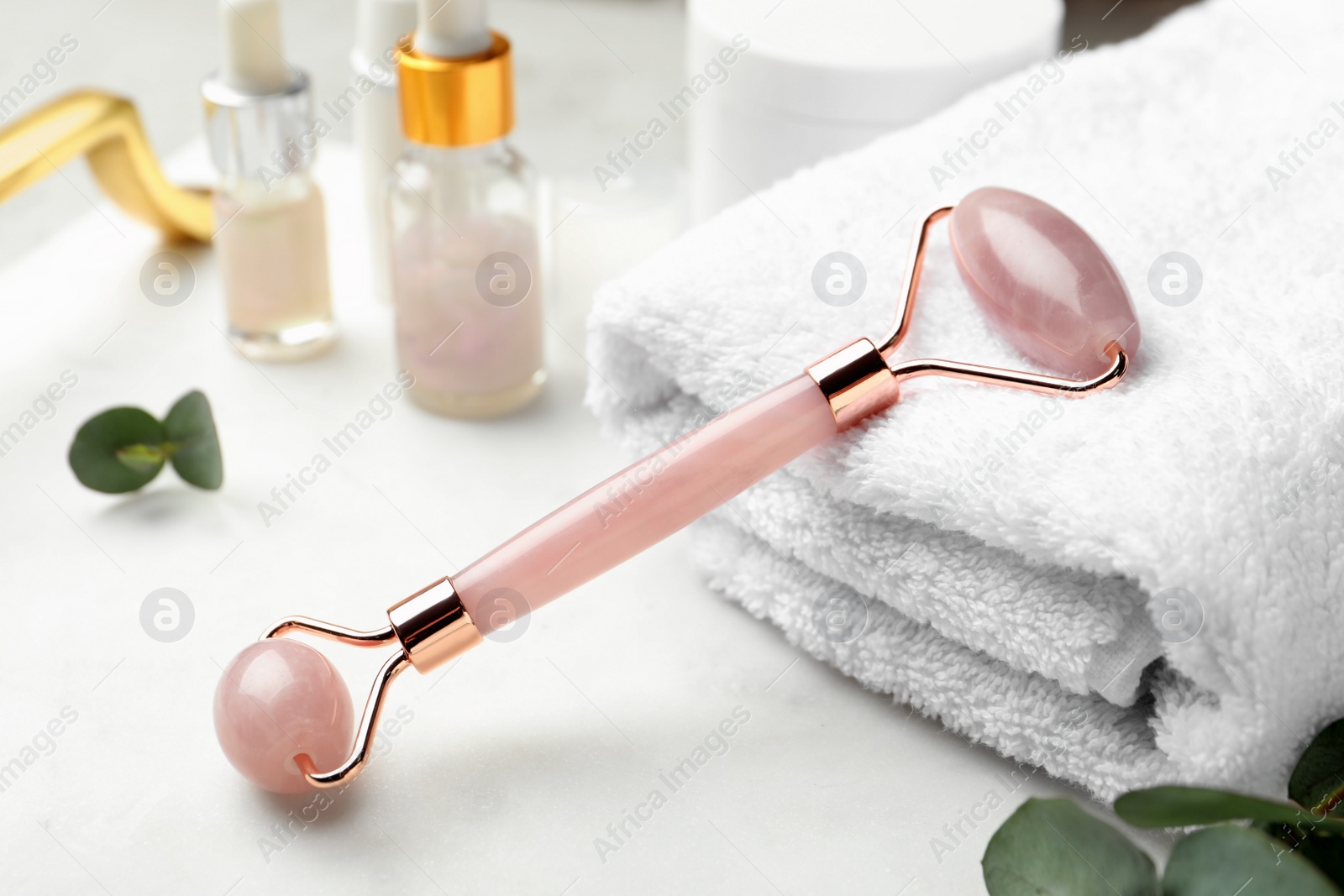 Photo of Natural face roller, towel and cosmetic products on light background