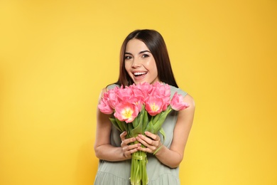 Photo of Portrait of beautiful smiling girl with spring tulips on yellow background. International Women's Day