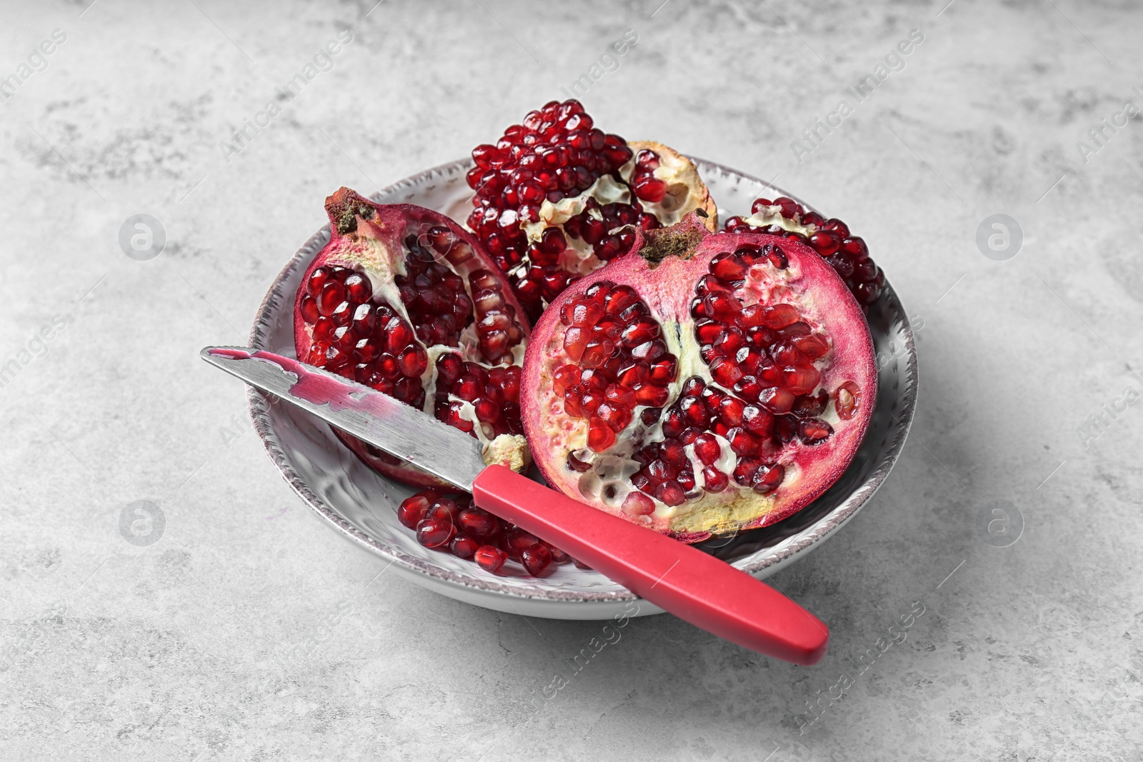 Photo of Plate with ripe pomegranates and knife on grey background