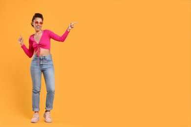 Photo of Happy young woman in stylish sunglasses dancing on orange background. Space for text