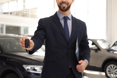 Salesman with key and clipboard in car salon, closeup