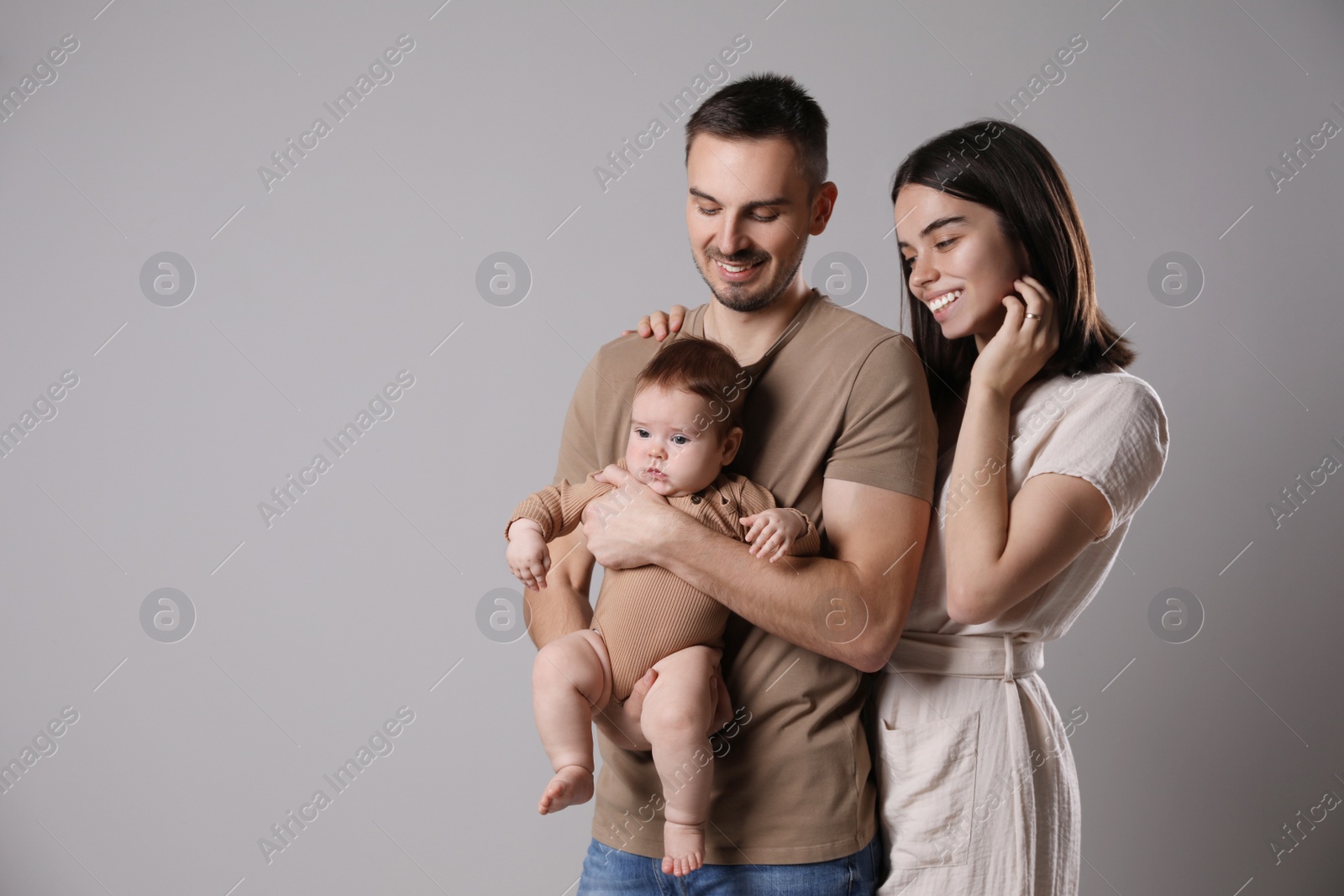 Photo of Happy family. Couple with their cute baby on grey background, space for text