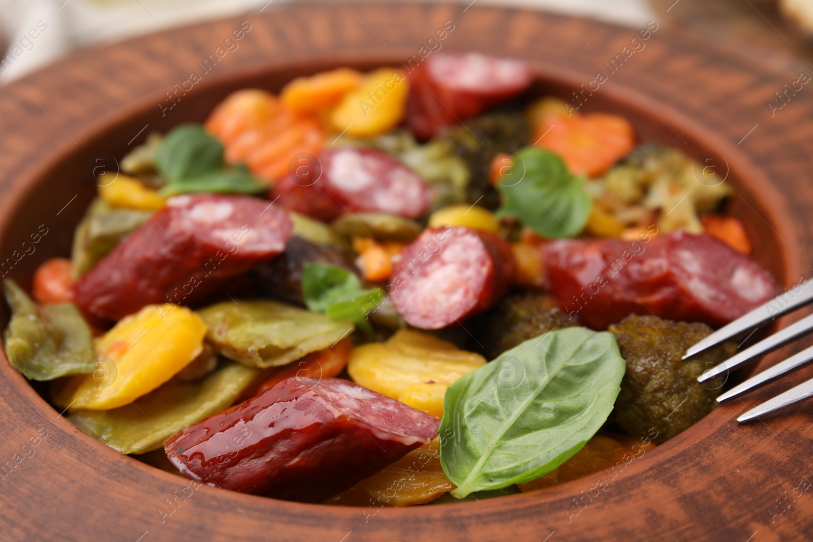 Photo of Delicious sausage and baked vegetables in bowl, closeup