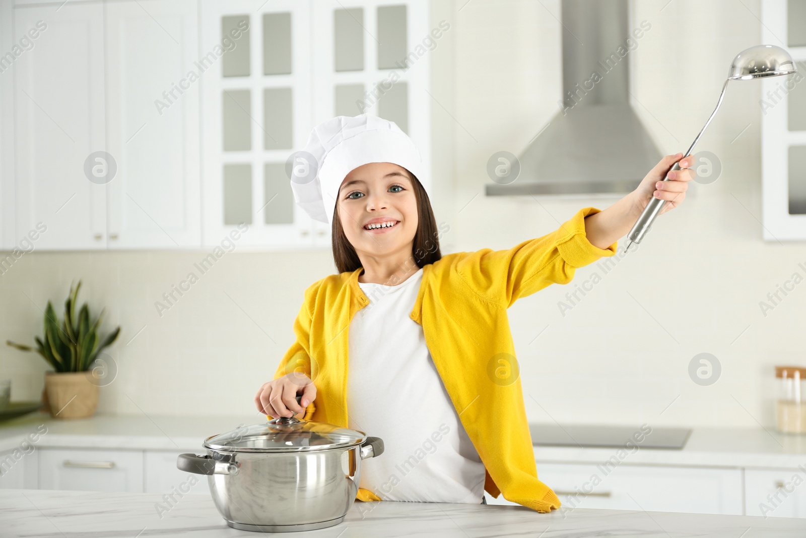 Photo of Cute little girl wearing chef hat with ladle in kitchen