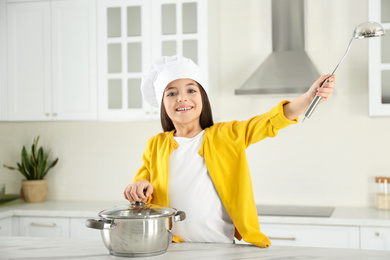 Cute little girl wearing chef hat with ladle in kitchen